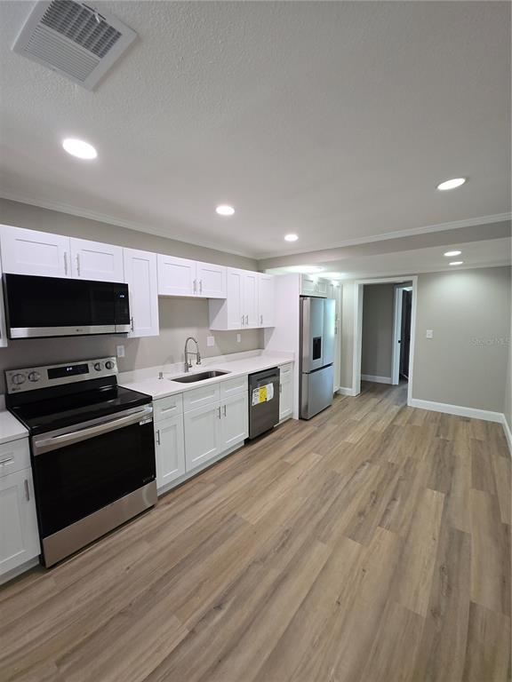 A kitchen with white cabinets, stainless steel appliances, and light wood-look flooring — 37406 VISTA DRIVE, DADE CITY, FL