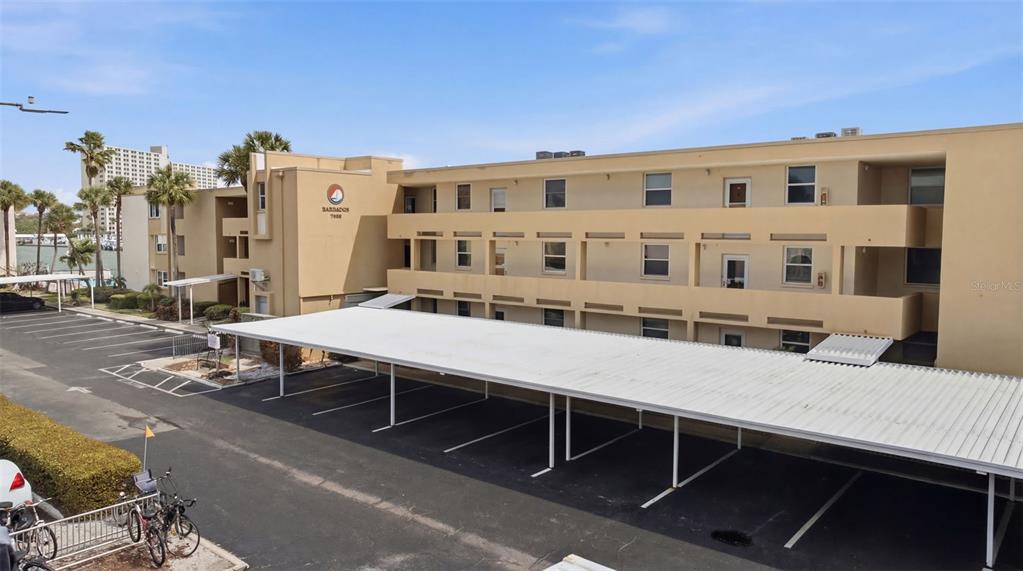 An exterior view of a multi-story apartment building with a covered parking area in front — 7465 BAY ISLAND DRIVE S UNIT 112, SOUTH PASADENA, FL