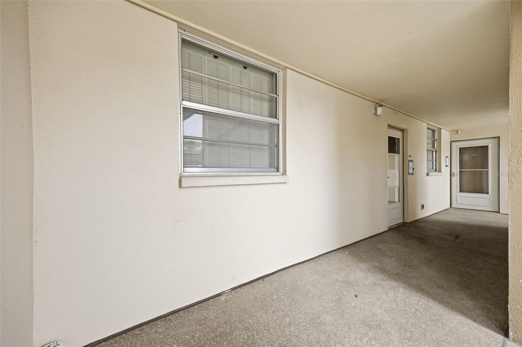 A covered exterior walkway features a window, a door, and a concrete floor — 7465 BAY ISLAND DRIVE S UNIT 112, SOUTH PASADENA, FL