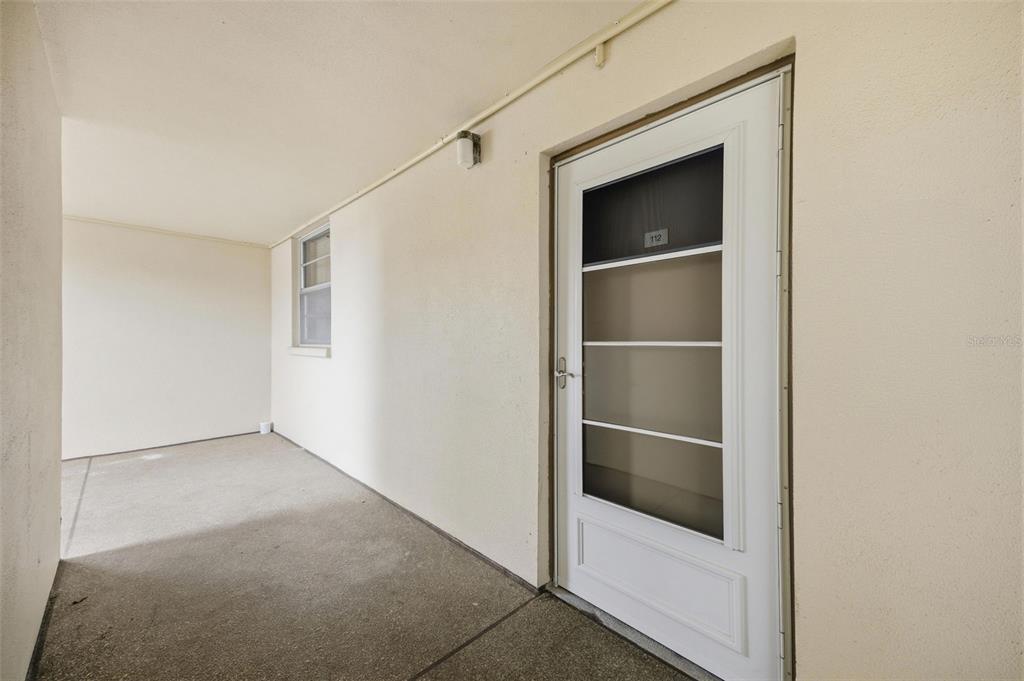 A concrete walkway leads to a white door with a screen and the number 112 — 7465 BAY ISLAND DRIVE S UNIT 112, SOUTH PASADENA, FL