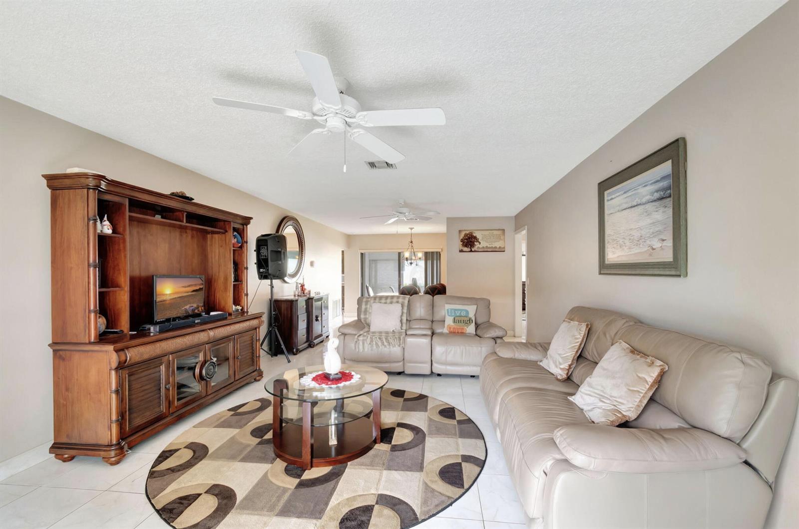 A living room features a large wooden entertainment center, leather sofas, and a circular rug — 4660 Greentree Place # 105b, Boynton Beach FL 33436, BOYNTON BEACH, FL
