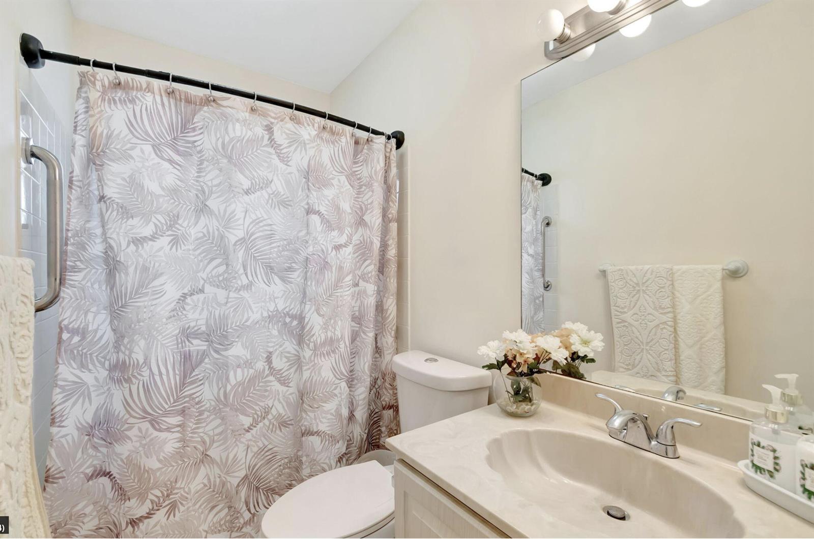 A bathroom features a vanity with a shell-shaped sink, a toilet, and a patterned shower curtain — 4660 Greentree Place # 105b, Boynton Beach FL 33436, BOYNTON BEACH, FL