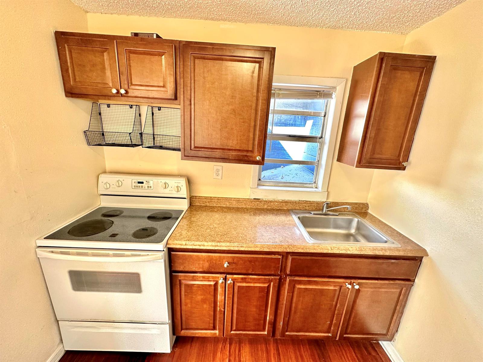 A small kitchen features wooden cabinets, a white electric stove, and a stainless steel sink — 517 Kanuga Drive Unit 3, West Palm Beach FL 33401, WEST PALM BEACH, FL