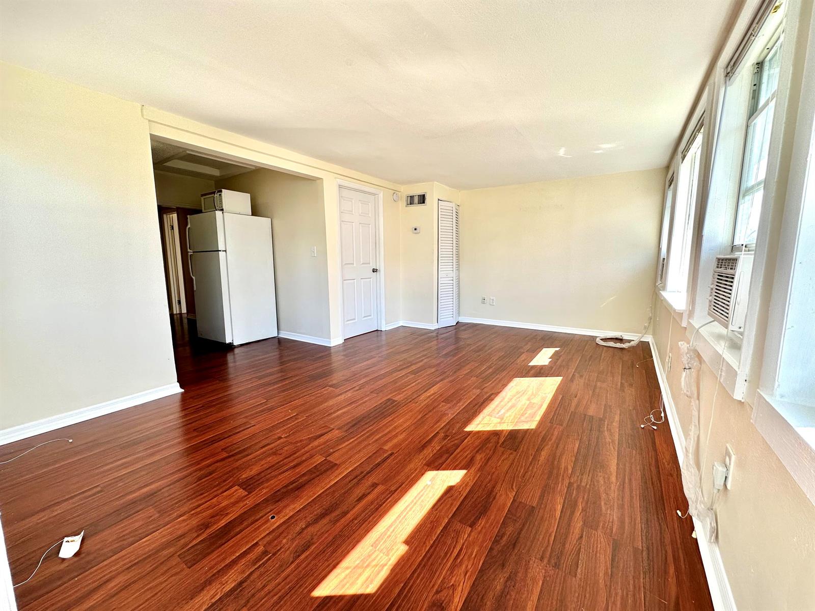 An empty living room with wood-look flooring, a white refrigerator, and a window air conditioner — 517 Kanuga Drive Unit 3, West Palm Beach FL 33401, WEST PALM BEACH, FL