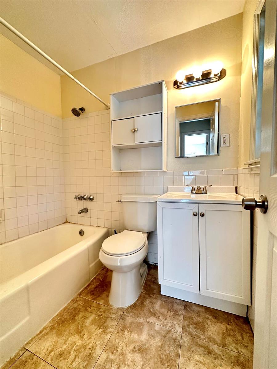 A bathroom features a tiled shower-tub combo, a white vanity, a toilet, and wall shelving — 517 Kanuga Drive Unit 3, West Palm Beach FL 33401, WEST PALM BEACH, FL