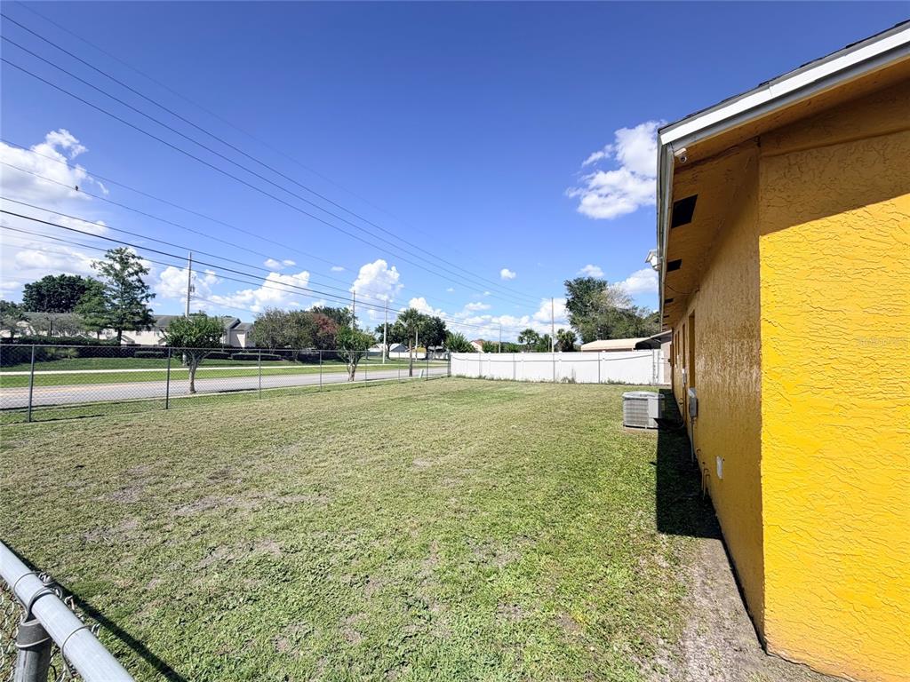 A side yard with a yellow stucco wall, a chain-link fence, and a white privacy fence — 5425 KAREN COURT, ORLANDO, FL