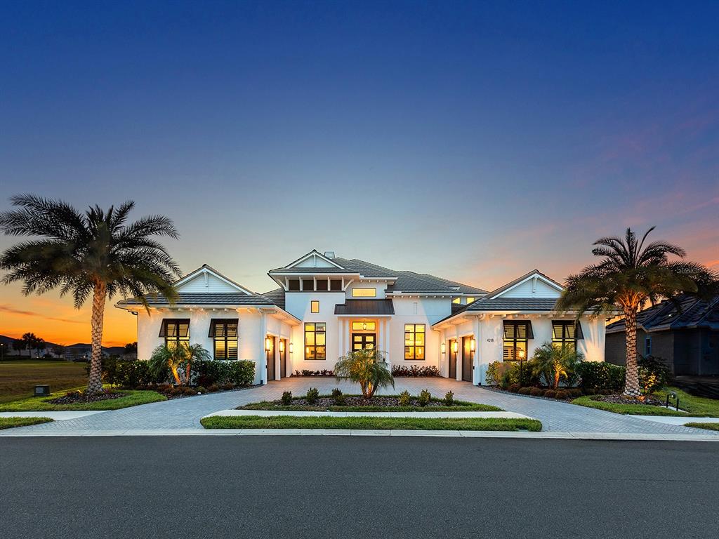 A modern white house with a multi-car garage and palm trees at sunset — 4218 BUTTE TRAIL, LAKEWOOD RANCH, FL