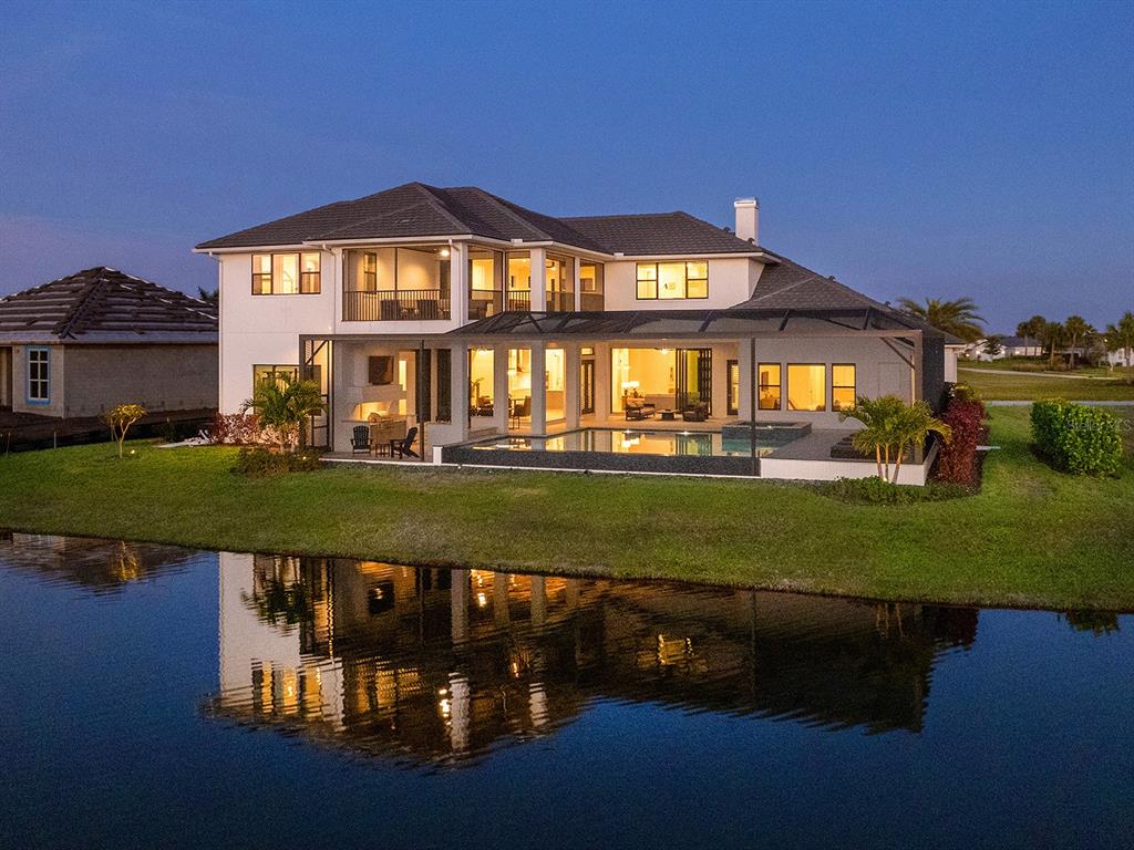 A two-story house with a screened-in pool and patio overlooking a lake at dusk — 4218 BUTTE TRAIL, LAKEWOOD RANCH, FL