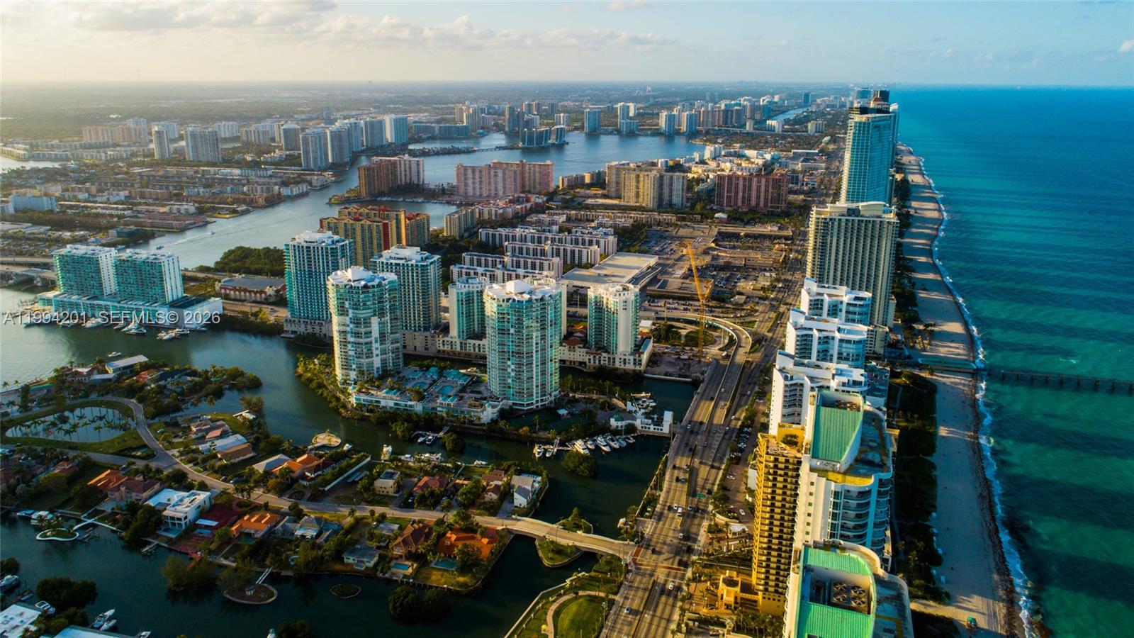 An aerial view of a coastal city featuring high-rise buildings, waterways, and a sandy beach — SUNNY ISLES BEACH, FL