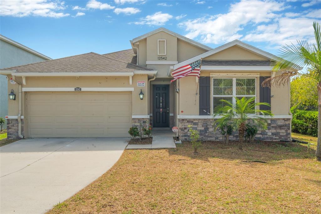 A single-story house with a beige stucco exterior, stone accents, and a two-car garage — 12542 CANDLEBERRY CIRCLE, TAMPA, FL