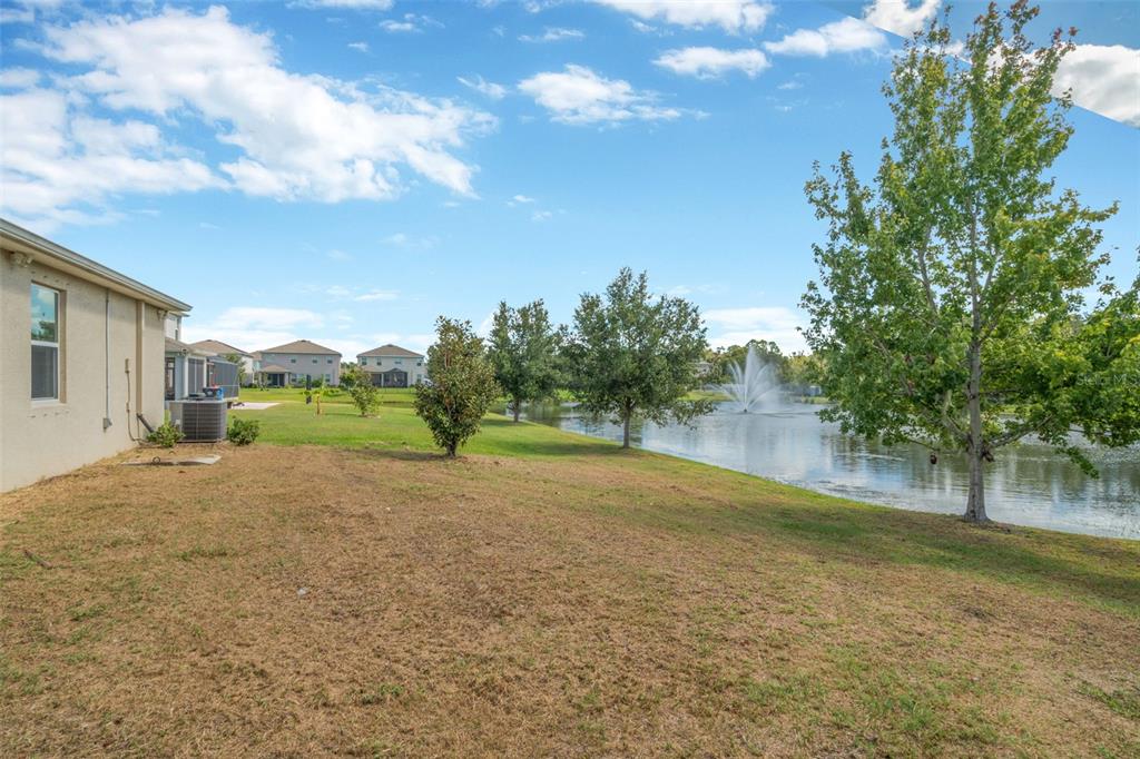A grassy backyard slopes toward a pond with a fountain behind a suburban house — 12542 CANDLEBERRY CIRCLE, TAMPA, FL