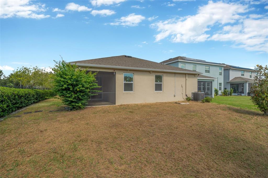 The exterior of a tan house features a screened-in patio and a large grassy backyard — 12542 CANDLEBERRY CIRCLE, TAMPA, FL