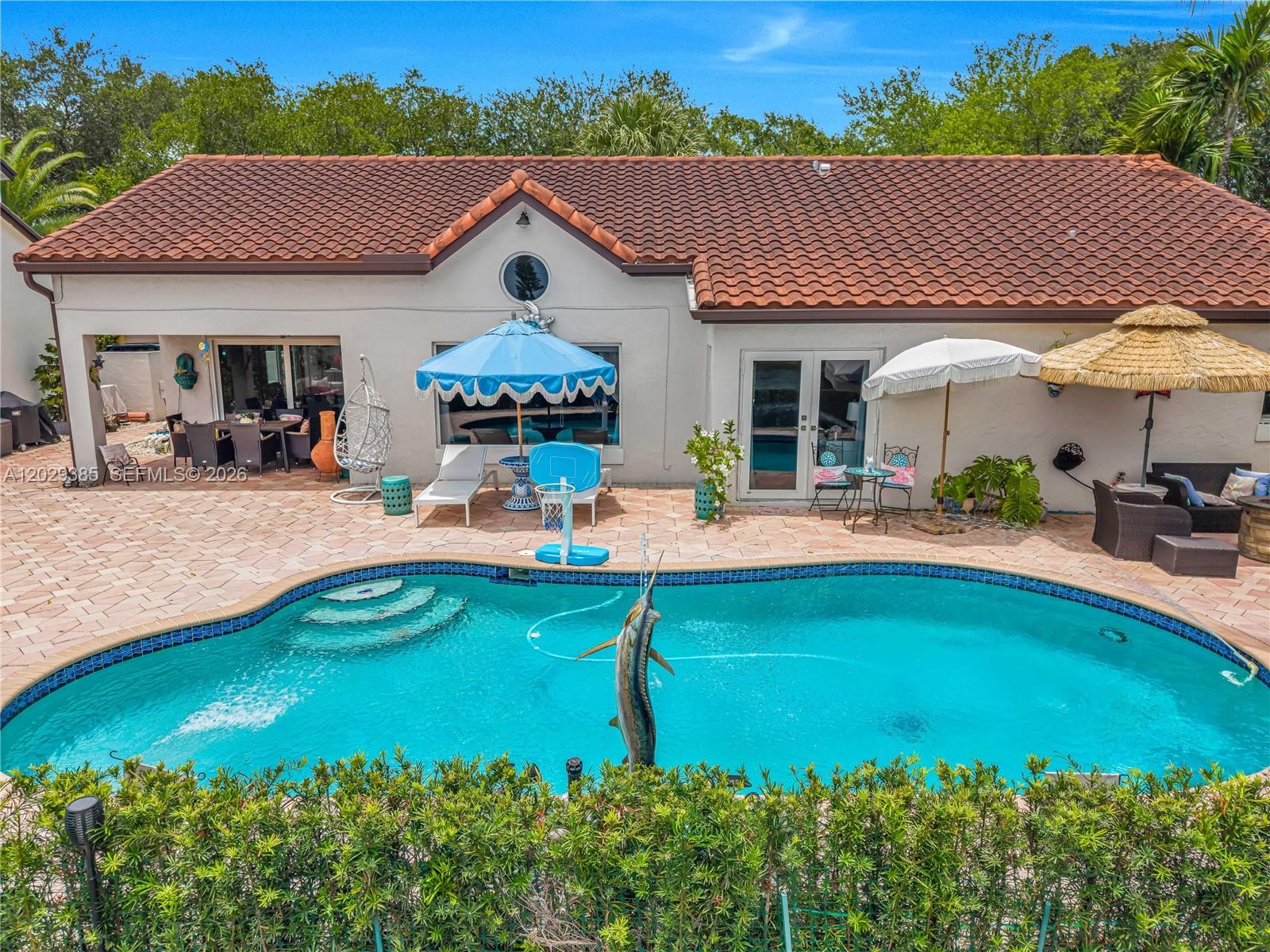 An outdoor patio features a swimming pool with a marlin fountain and multiple umbrellas — 19641 NW 88th Ave, Hialeah FL 33018, HIALEAH, FL