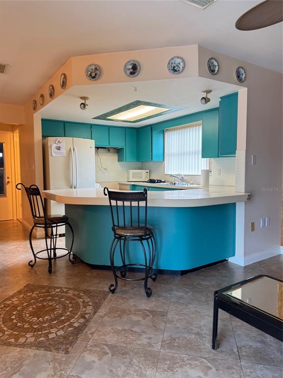 A kitchen features teal cabinets, a white countertop, and two black metal bar stools — 9201 BARRINGTON LANE, PORT RICHEY, FL
