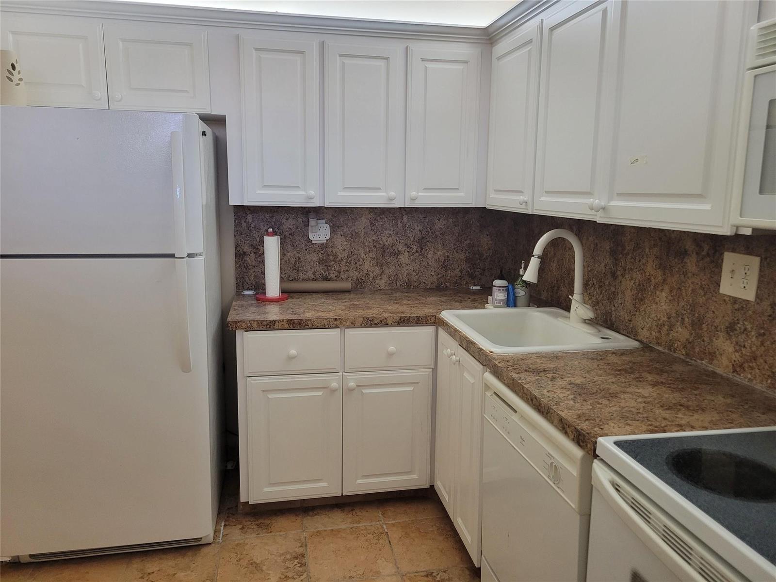 A kitchen features white cabinets, a brown laminate countertop, a white sink, and white appliances — 3671 Environ Boulevard # 468, Lauderhill FL 33319, LAUDERHILL, FL