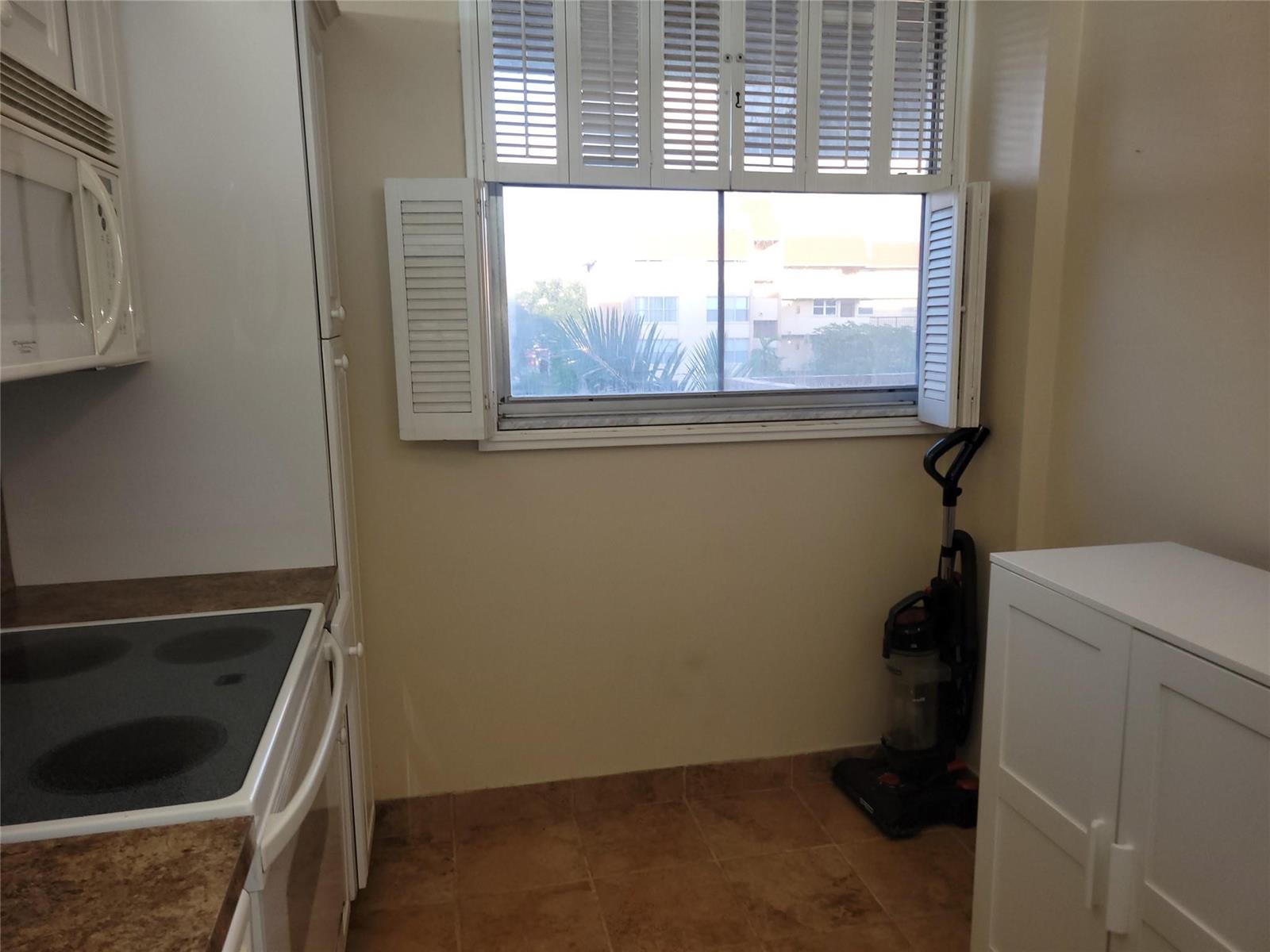 A kitchen area features a stove, a window with shutters, and a vacuum cleaner — 3671 Environ Boulevard # 468, Lauderhill FL 33319, LAUDERHILL, FL