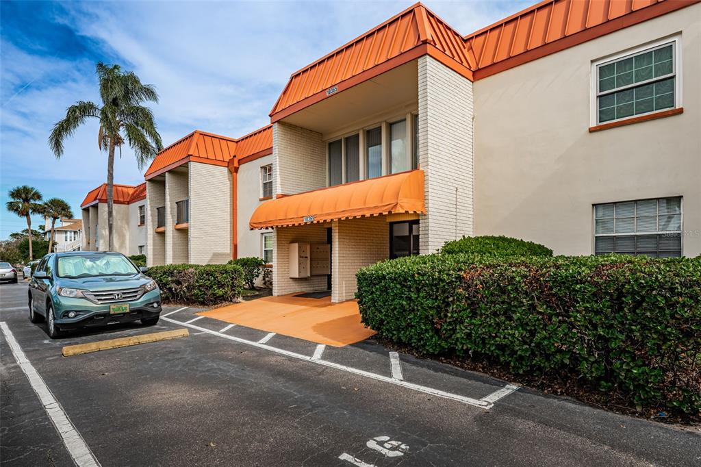 A two-story apartment building features white brick walls, orange metal roofs, and a covered entrance — 10365 PARADISE BOULEVARD UNIT 16, TREASURE ISLAND, FL