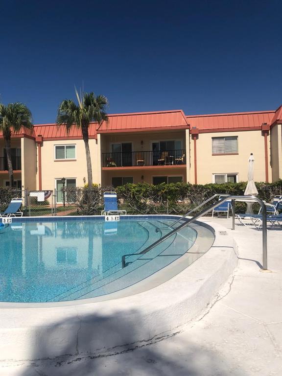 A swimming pool with steps and a metal handrail sits in front of a two-story building — 10365 PARADISE BOULEVARD UNIT 16, TREASURE ISLAND, FL