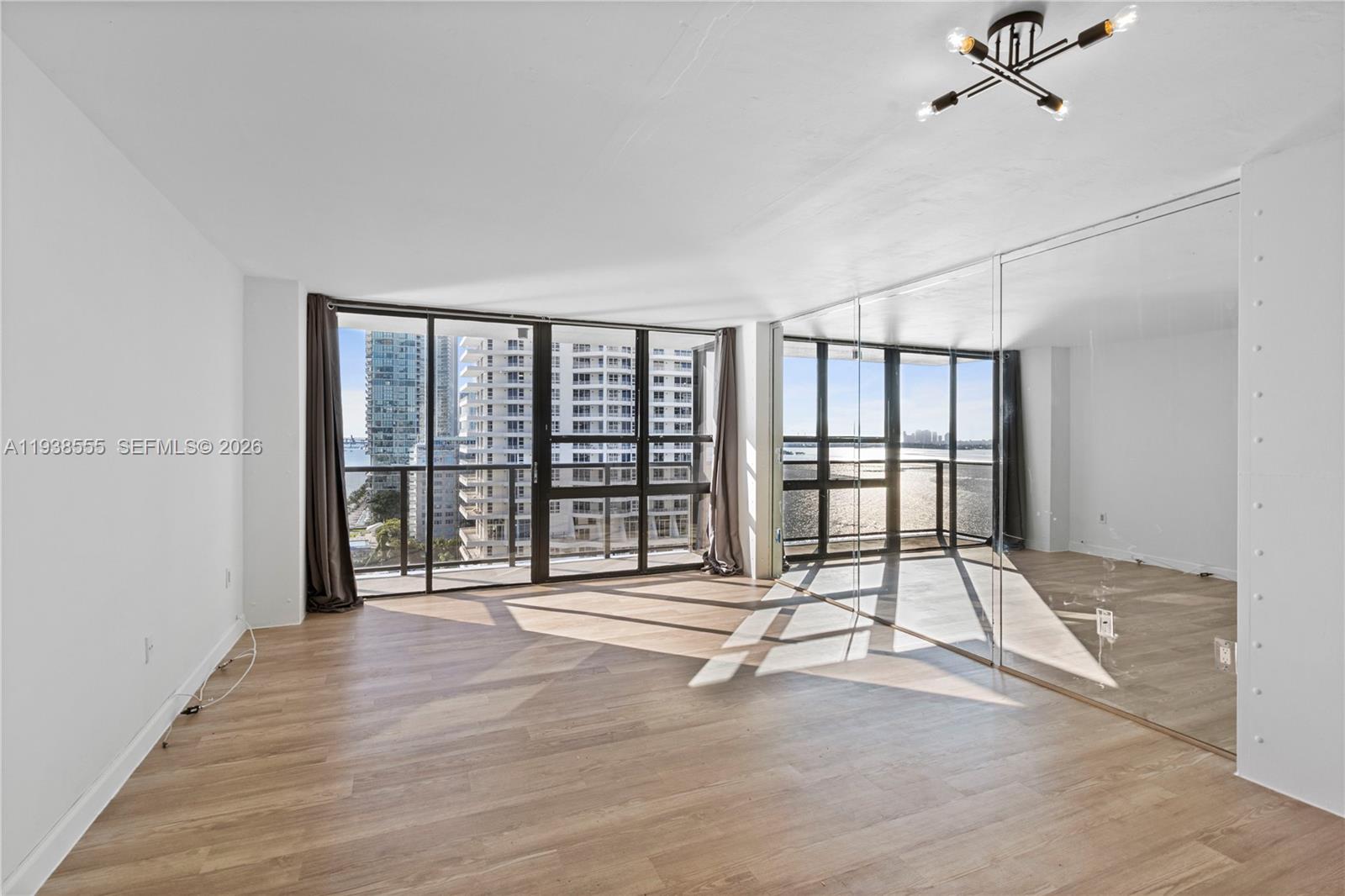 A bright living area features light wood flooring, floor-to-ceiling windows, and a mirrored wall — 600 NE 36th St # 1520, Miami FL 33137, MIAMI, FL