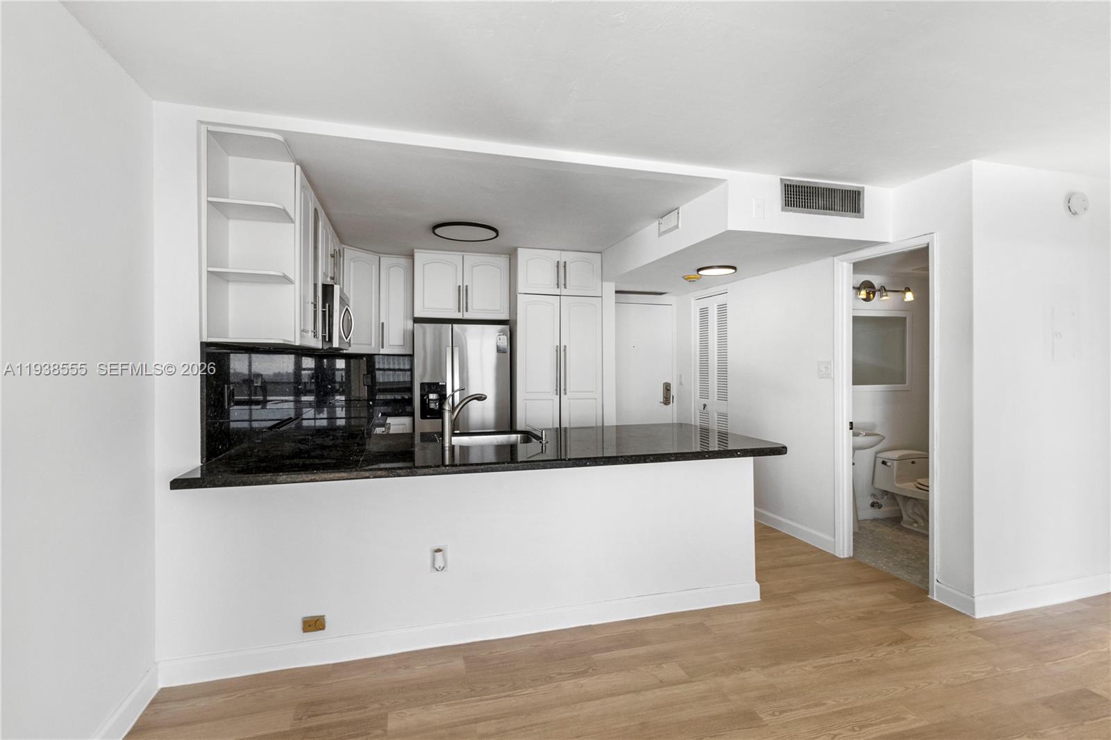 A kitchen with white cabinets and black countertops overlooks an open living area — 600 NE 36th St # 1520, Miami FL 33137, MIAMI, FL