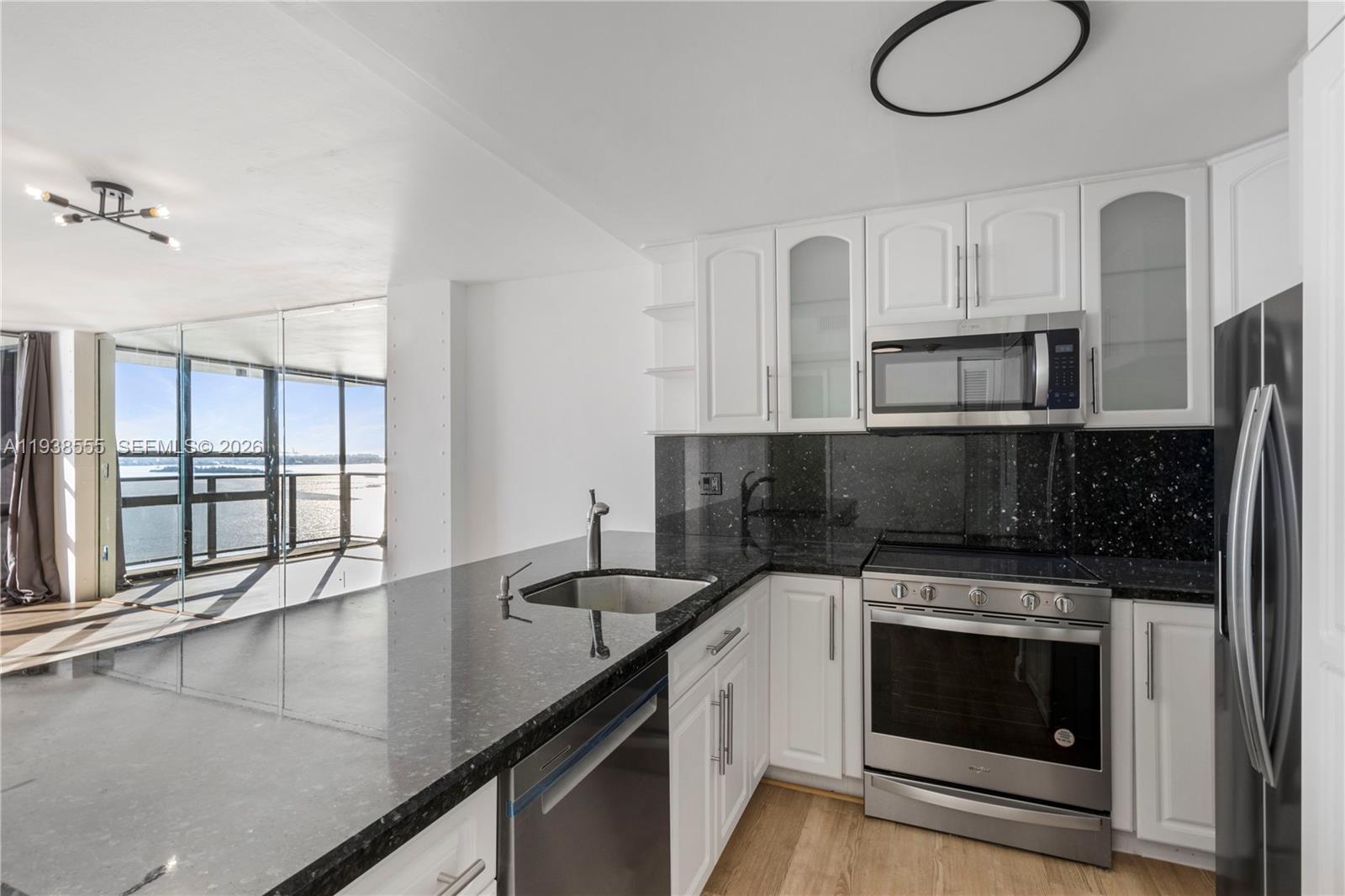 A kitchen with white cabinets, black granite countertops, and stainless steel appliances overlooks a balcony — 600 NE 36th St # 1520, Miami FL 33137, MIAMI, FL