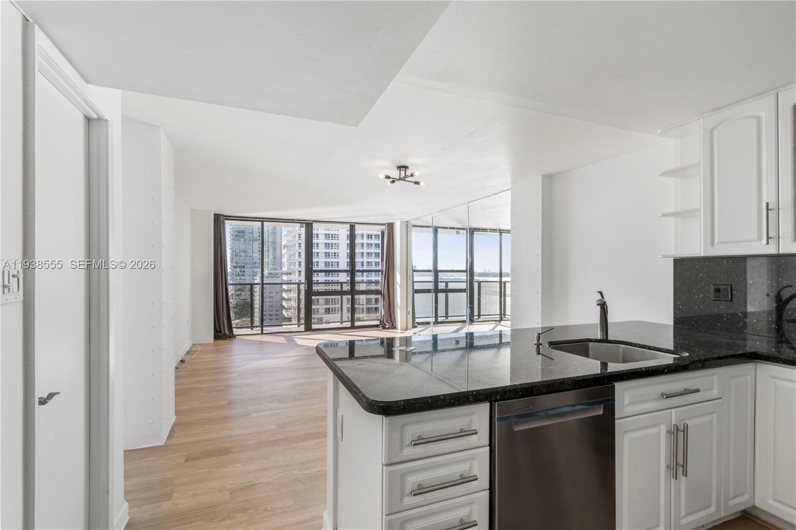 A kitchen with dark granite countertops and white cabinets overlooks an open living area — 600 NE 36th St # 1520, Miami FL 33137, MIAMI, FL