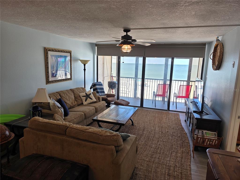 A living room features a tan sofa, a coffee table, and sliding doors opening to a balcony — 17580 GULF BOULEVARD UNIT 311, REDINGTON SHORES, FL