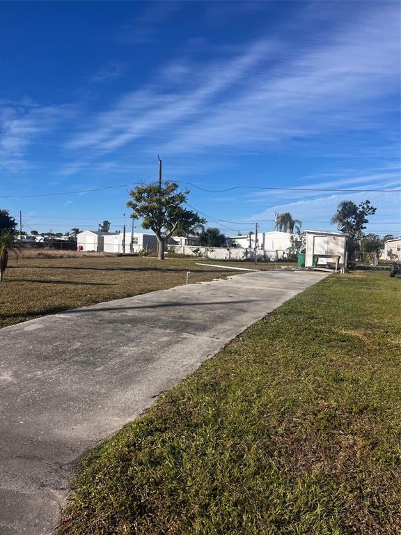 A concrete driveway leads toward a small shed on a grassy lot under a blue sky — 1348 FLAMINGO DRIVE, ENGLEWOOD, FL