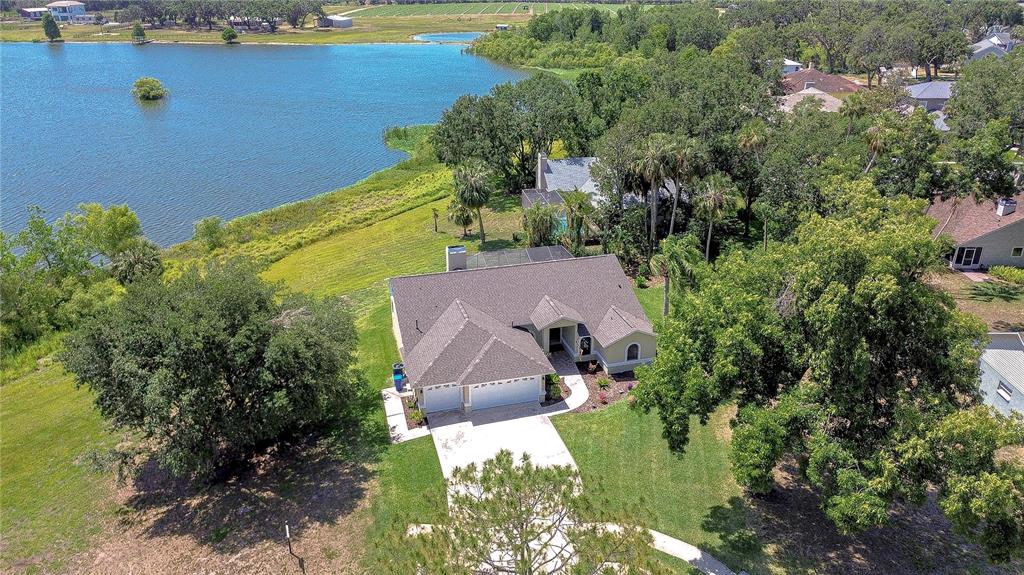 An aerial view shows a single-story house with a gray roof situated near a lake — 709 SPORTSMAN PARK DRIVE, SEFFNER, FL