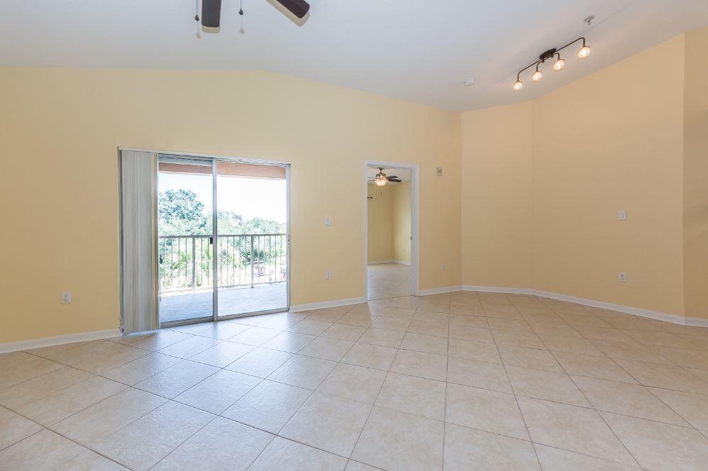 An empty living room features beige tile flooring, yellow walls, and a sliding glass door — 5080 Fairways Circle # G301, Vero Beach FL 32967, VERO BEACH, FL