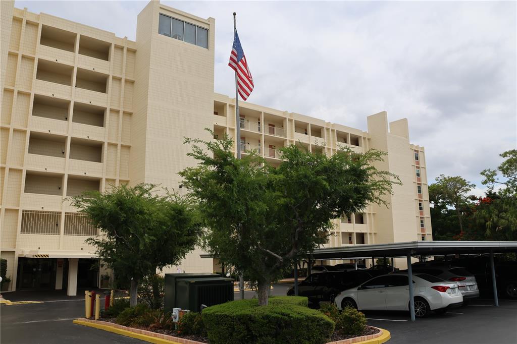 A multi-story beige apartment building features a flag pole and a covered parking area — 700 MIRROR TERRACE NW UNIT 303, WINTER HAVEN, FL