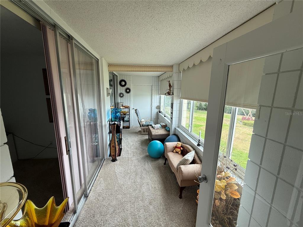 A carpeted sunroom features sliding glass doors, large windows, and a small beige sofa — 700 MIRROR TERRACE NW UNIT 303, WINTER HAVEN, FL