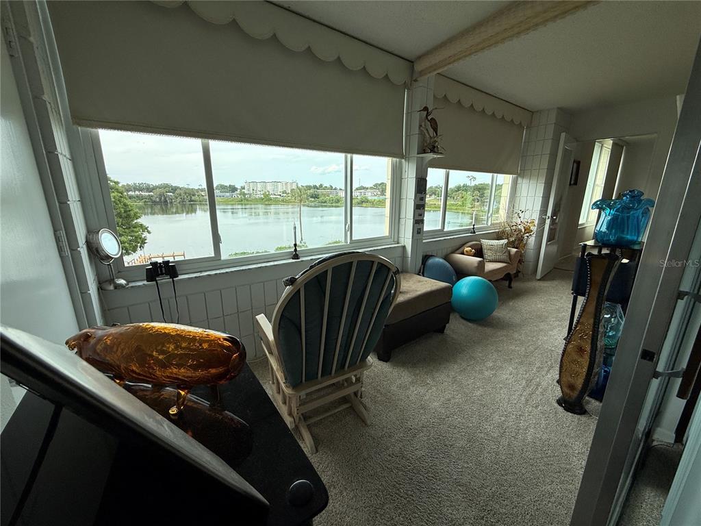 A sunroom with carpeted floors, a rocking chair, and large windows overlooking a lake — 700 MIRROR TERRACE NW UNIT 303, WINTER HAVEN, FL