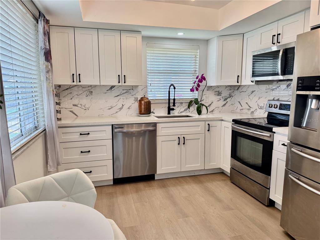 A kitchen with white cabinets, marble-patterned backsplash, stainless steel appliances, and light wood-look flooring — 5440 RIVERBLUFF CIRCLE UNIT 87, SARASOTA, FL