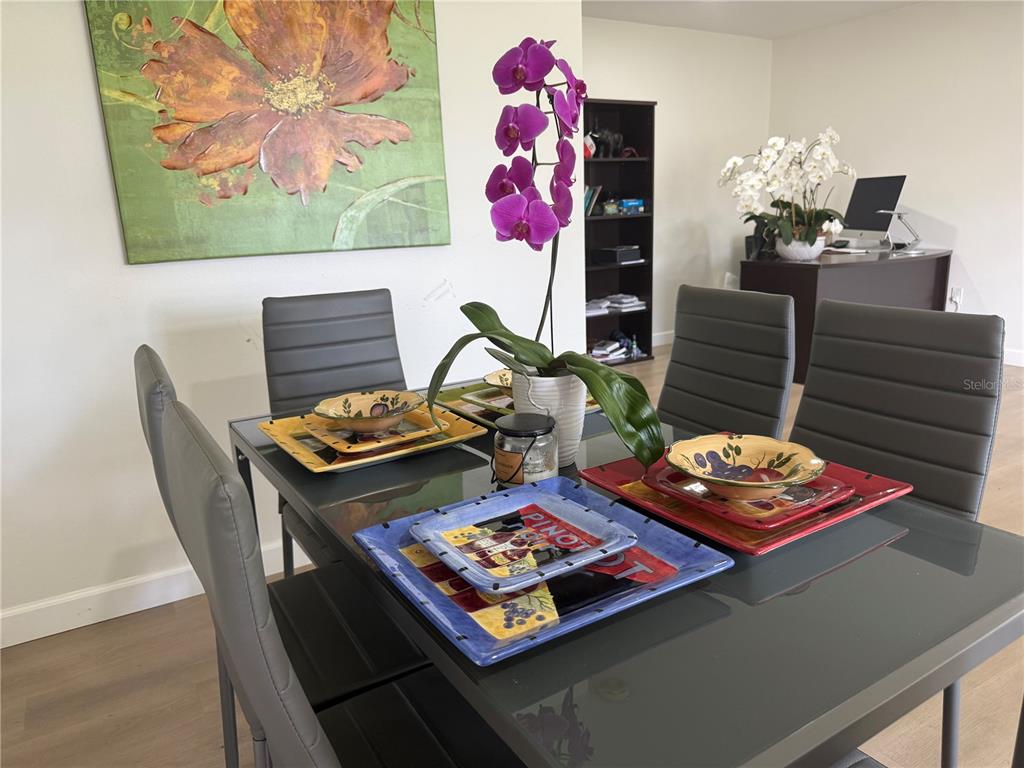 A dining room features a glass-topped table with grey chairs and colorful place settings — 5440 RIVERBLUFF CIRCLE UNIT 87, SARASOTA, FL