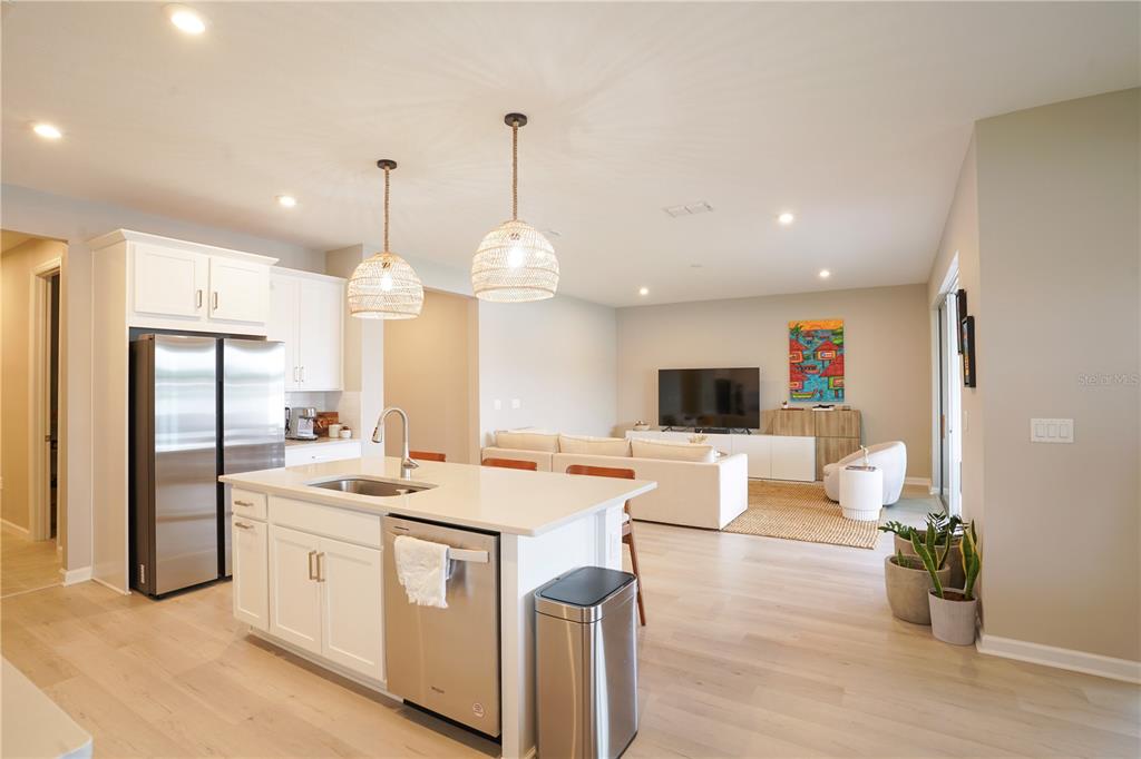 A modern open-concept kitchen with white cabinets and an island overlooks a living room area — 7964 WATERFIELD AVENUE, ORLANDO, FL