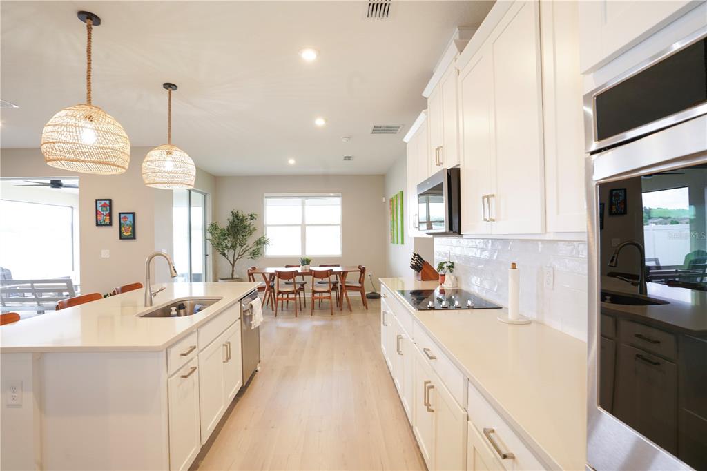 A modern kitchen features white cabinetry, a central island with a sink, and pendant lighting — 7964 WATERFIELD AVENUE, ORLANDO, FL