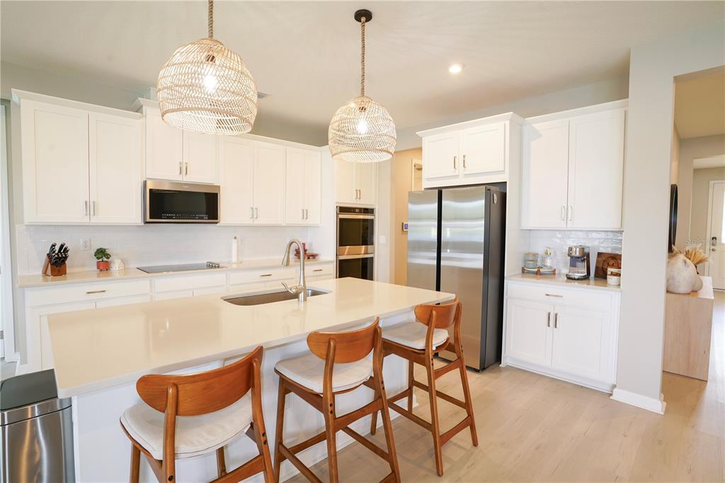 A modern kitchen features white cabinetry, a large quartz island, and two woven pendant lights — 7964 WATERFIELD AVENUE, ORLANDO, FL
