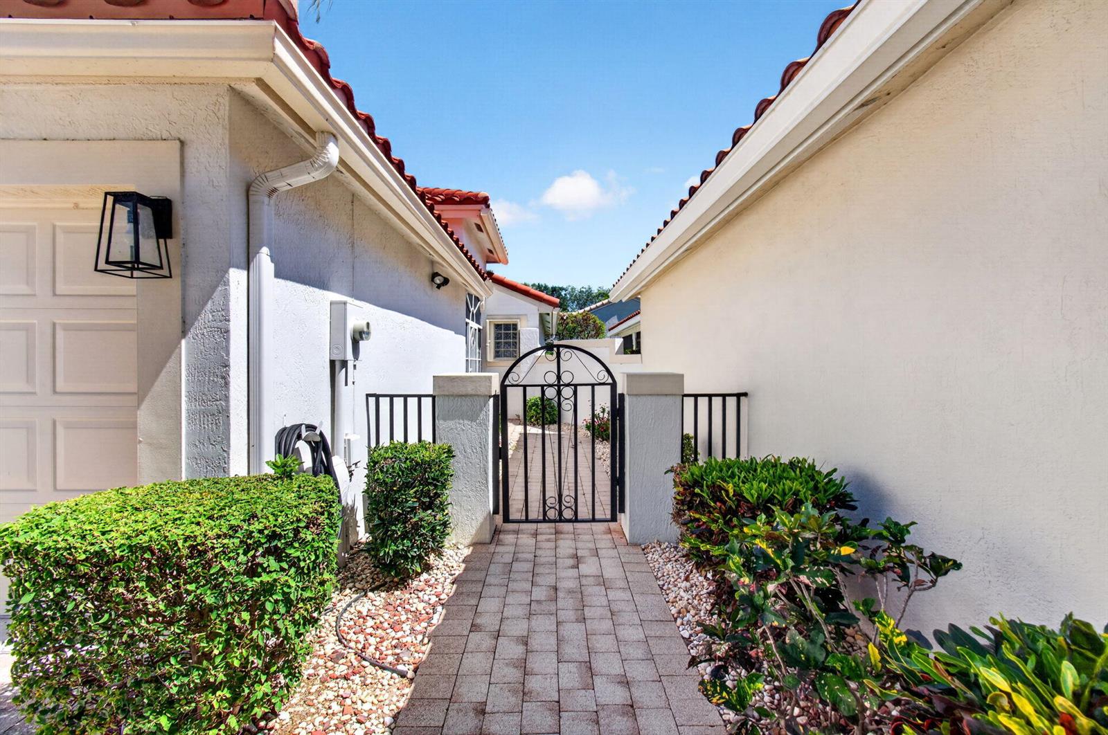 A paved walkway leads to a metal gate between two stucco houses with tiled roofs — 7169 Foxworth Court, Boynton Beach FL 33437, BOYNTON BEACH, FL