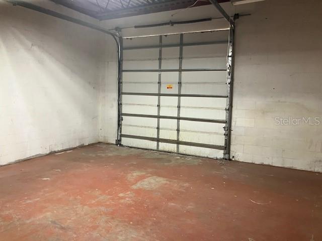 An interior view of a garage with white concrete block walls and a red floor — 5001 S MACDILL AVENUE UNIT 100, TAMPA, FL