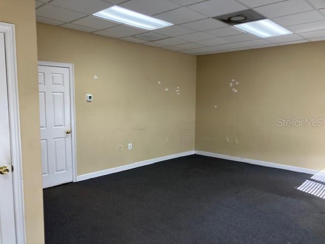 An empty office room features beige walls, dark carpeting, and a white door — 5001 S MACDILL AVENUE UNIT 100, TAMPA, FL