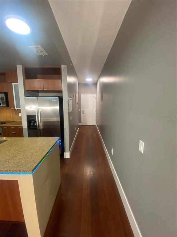 A kitchen with wood cabinets and a stainless steel refrigerator opens into a long hallway — 111 N 12TH STREET UNIT 1411, TAMPA, FL