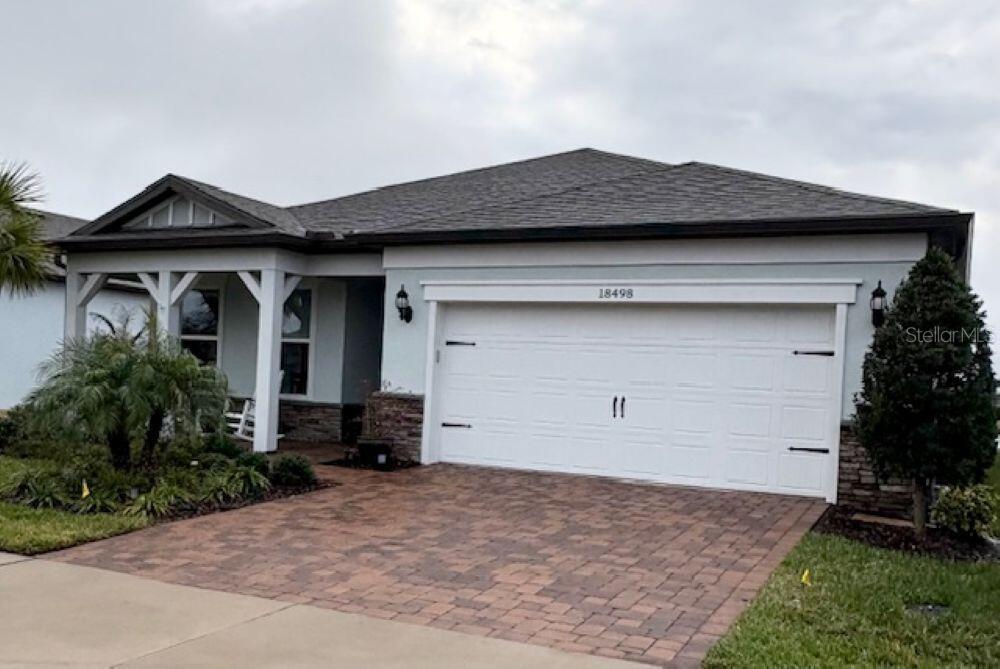 A single-story house features a white garage, stone accents, and a covered front porch — 18498 COASTAL SHORE TERRACE, LAND O LAKES, FL