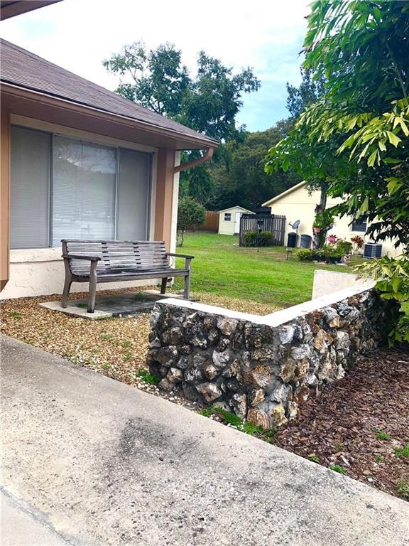A wooden bench sits on a gravel patio next to a stone wall outside a house — 5806 MARBLE COURT, WINTER PARK, FL
