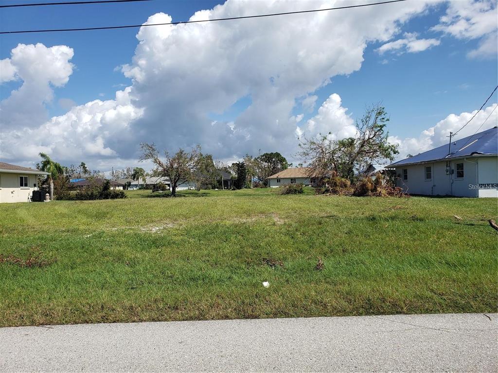 A vacant, grassy residential lot sits between two existing houses under a cloudy blue sky — 191 BUNKER ROAD, ROTONDA WEST, FL