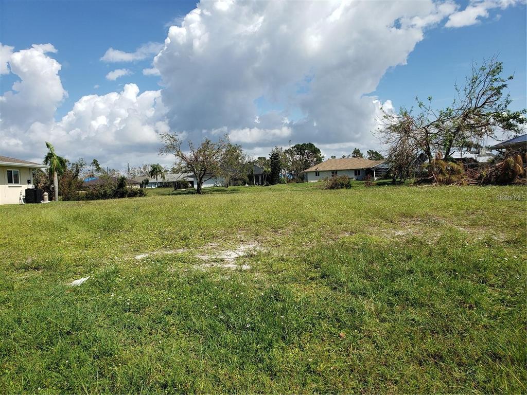 A grassy, vacant lot is shown with neighboring houses and trees under a cloudy sky — 191 BUNKER ROAD, ROTONDA WEST, FL