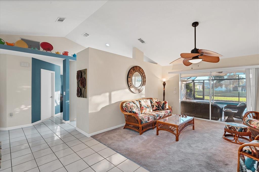 A living room with a vaulted ceiling, rattan furniture, and a sliding door to a pool — 25 FAIRWAY ROAD, ROTONDA WEST, FL