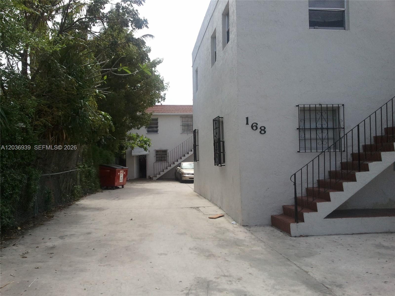 An exterior view shows two white apartment buildings with outdoor staircases and a concrete driveway — 168 NW 32nd St # 6, Miami FL 33127, MIAMI, FL