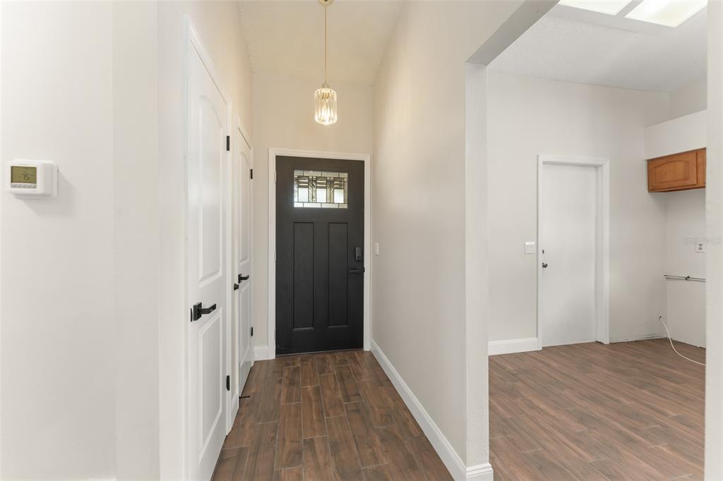 An entryway features a black front door, wood-look tile flooring, and a hanging pendant light — 2458 LONG MEADOW WAY, ORLANDO, FL