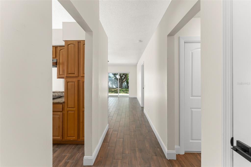 A hallway with wood-look tile flooring leads toward a glass sliding door viewing the outdoors — 2458 LONG MEADOW WAY, ORLANDO, FL